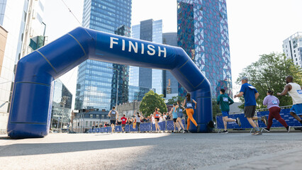 Smiling Group of People Participating in a City Marathon. Wide Shot of Diverse Race Runners Reaching the Finish Line, Celebrating Their Victory and Achieving their Goal - obrazy, fototapety, plakaty