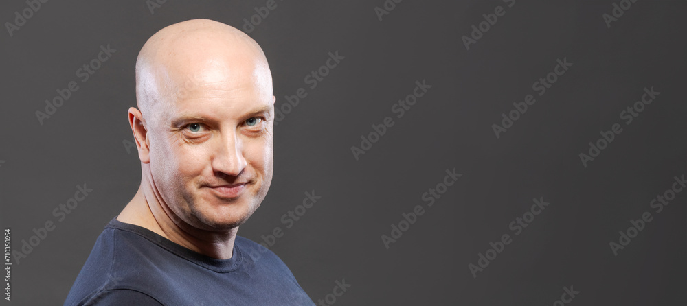 Wall mural bald adult man on a dark background looking at the camera.