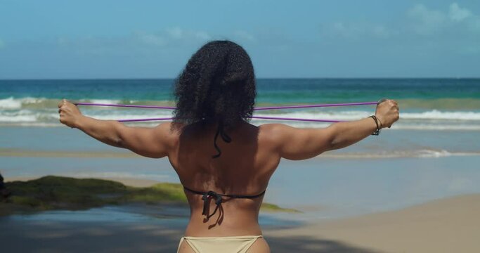 Picture a determined fitness girl sculpting her physique in a bikini at an amazing outdoor tropical beach location.