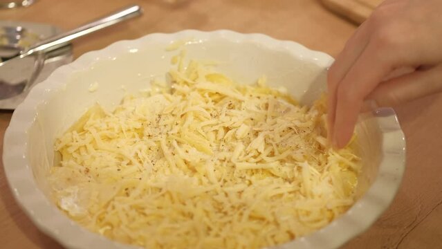 A woman sprinkles cheese on potatoes for baking. Prepare gratin dauphinois