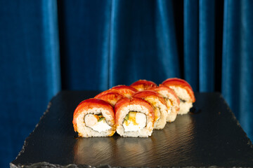Sushi set on blue velvet background. Maki roll with salmon and eel on black slate. Modern, stylish Japanese cuisine. Sushi restaurant menu.