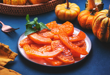 Healthy sweet snack. Baked pumpkin caramelized in orange glaze, autumn or winter dessert food on dark green table background. Top view