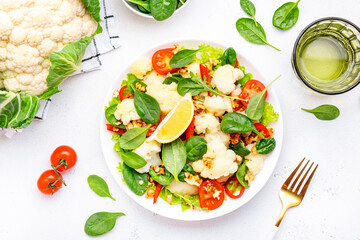 Fresh vegan cauliflower salad with baked red paprika, cherry tomatoes, spinach with walnuts on white table background, top view