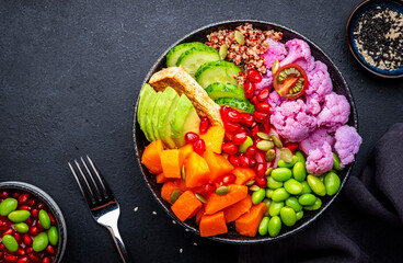 Vegan buddha bowl with pumpkin, quinoa, avocado, edamame, tofu, cauliflower, pomegranate and seeds, black table background, top view. Healthy vegetarian comfort food