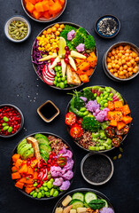 Vegan buddha bowls set with pumpkin, quinoa, tomatoes, spinach, avocado, radish, soybeans, tofu, cabbage and seeds on black table background, top view. Healthy menu, vegetarian comfort food