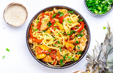 Stir fryed egg noodles with chicken, fresh pineapple, paprika, green onion, ginger, garlic, soy sauce and sesame seeds in bowl. Asian cuisine dish. White table background, top view