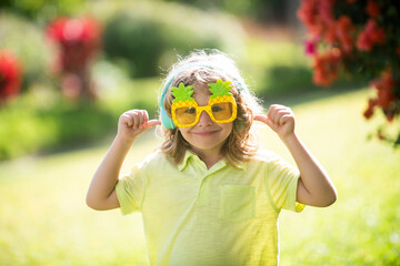 Excited kid boy with headphones and funny sunglasses. Portrait of kid in spring park outdoors. Close-up face child playing outdoors in summer park.