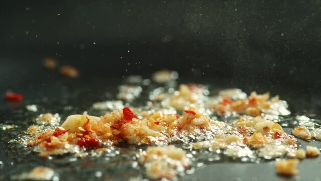 Close up Slow motion Chopped Garlic and red chili frying with boiling oil in black teflon pan 4k