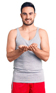 Young handsome man wearing swimwear and sleeveless t-shirt smiling with hands palms together receiving or giving gesture. hold and protection