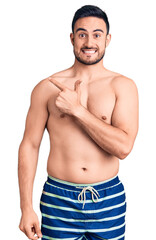Fototapeta premium Young handsome man wearing swimwear cheerful with a smile on face pointing with hand and finger up to the side with happy and natural expression