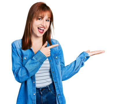 Redhead young woman wearing casual denim jacket amazed and smiling to the camera while presenting with hand and pointing with finger.