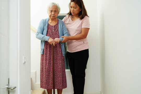 Asian senior woman use walking stick with caregiver help support walking down the stairs prevent accident, slip and fall at home.