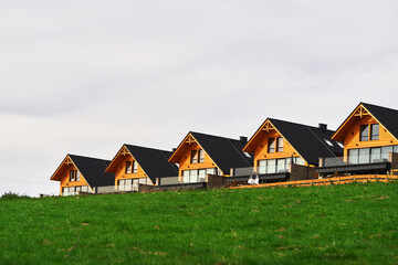 Modern wooden houses on a green hill with a stunning view of the sky and the fields. A row of modern wooden houses and green grass foreground.