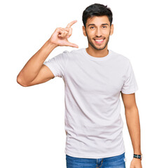 Young handsome man wearing casual white tshirt smiling and confident gesturing with hand doing small size sign with fingers looking and the camera. measure concept.