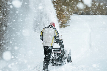 Man removes snow with a snowblower rear view. working with a gasoline snow blower after the severe winter storm in the city. Clearing the area from snowfall.