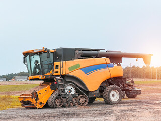 farming vehicle called a combine harvester is parked on a field of soil. It is used to harvest crops and separate the grains from the straw.
