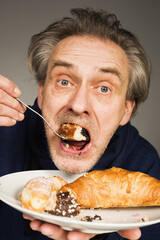 Older man eating sweet pastry and cakes as a meal in studio