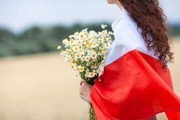 Close up of woman with bouquet of daisies covered with flag of Poland in wheat field. Polish Flag...