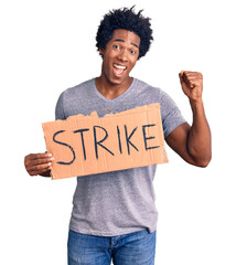 Handsome african american man with afro hair holding strike banner cardboard screaming proud, celebrating victory and success very excited with raised arms