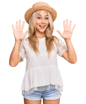 Young blonde girl wearing summer hat showing and pointing up with fingers number ten while smiling confident and happy.