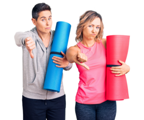 Couple of women holding yoga mat with angry face, negative sign showing dislike with thumbs down, rejection concept