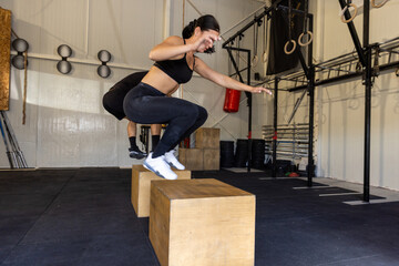 Fitness couple are performing box jumps at gym, plyometric exercise