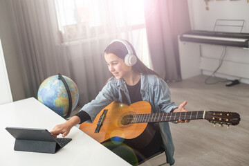 Latin girl with headphones listening to her online music lessons. Artistic kid playing the acoustic...