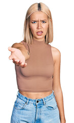 Fototapeta premium Beautiful young blonde woman offering hand clueless and confused expression. doubt concept.