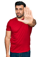 Hispanic man with beard wearing casual red t shirt doing stop sing with palm of the hand. warning expression with negative and serious gesture on the face.