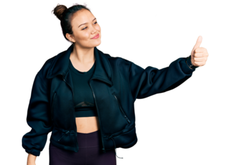 Young hispanic girl wearing sportswear looking proud, smiling doing thumbs up gesture to the side