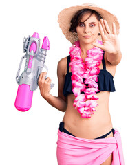 Beautiful young woman with short hair wearing bikini and hawaiian lei holding water gun with open...