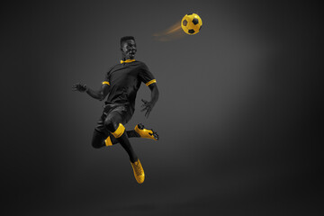 Black and yellow color combination. Young African man, football player in motion kicking ball with...