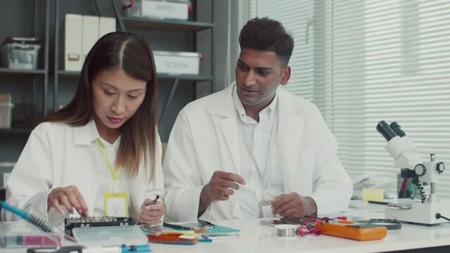 Medium shot of two repair center workers discussing how to fix broken component of device sitting at tableMedium shot of two repair center workers discussing how to fix broken component of device sitt