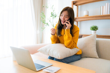 Young Asian female wearing glasses using laptop, working at home in living room, coffee mug on table. Cozy office workplace, remote work