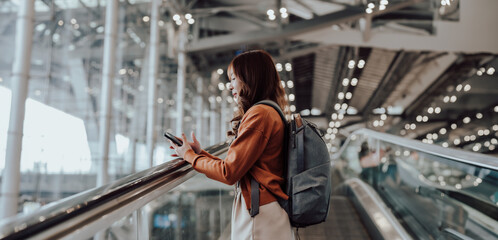 Fototapeta premium Young asian woman in international airport terminal or modern train station. Backpacker passenger female commuter walking on escalator