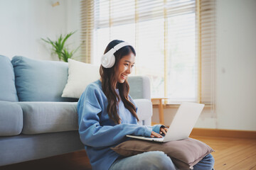 Young asian woman smile wearing headset working in living room at home. Happy female using computer...