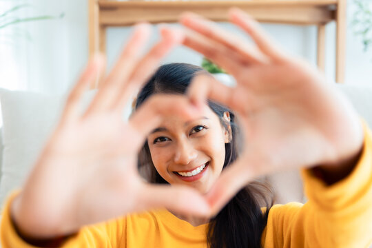 Front view of cute young Asian woman smiling and looking at camera with hands showing heart shape. Facial expressions and positive emotions, healthy life, love and charity