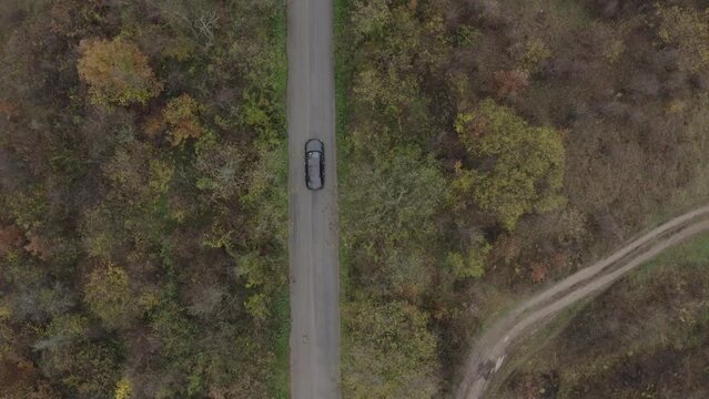 Retreating follow-through drone shot of a moving vehicle on a road located at the foot of the Balkan Mountains in Bulgaria.