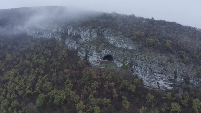 A view from afar through a drone shot of Kozarnika Cave, located in the Balkan Mountain range in Dimovo Municipality, Bulgaria.