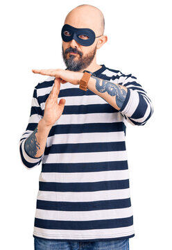 Young handsome man wearing burglar mask doing time out gesture with hands, frustrated and serious face