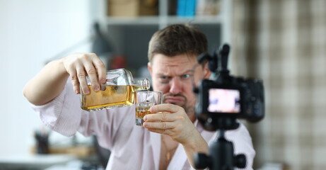 Man with hematoma under his eye pouring alcohol and taking video camera. Opportunities to make money on internet concept