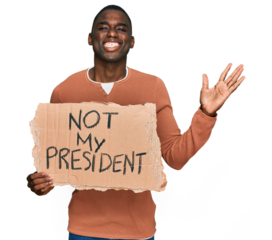 Young african american man holding not my president protest banner celebrating victory with happy smile and winner expression with raised hands