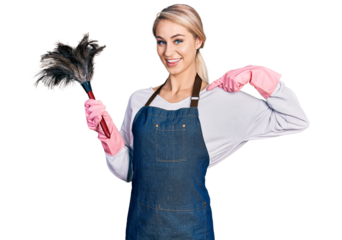 Beautiful young blonde woman wearing apron holding cleaning duster looking confident with smile on face, pointing oneself with fingers proud and happy.