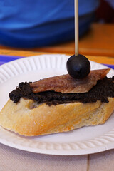 Close up baguette bread toast topped with Black Olive Tapenade spread and Marinated Anchovy fish