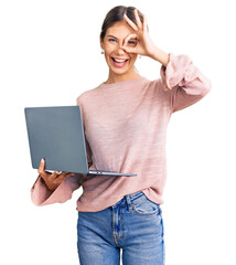 Beautiful caucasian woman with blonde hair working using computer laptop smiling happy doing ok sign with hand on eye looking through fingers
