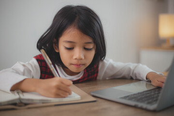 Naklejka premium Cute and happy little Asian girl children using a laptop computer, studying through an online e-learning system at home.