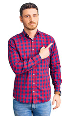 Fototapeta na wymiar Handsome young man with bear wearing casual shirt pointing with hand finger to the side showing advertisement, serious and calm face