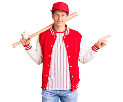 Young handsome man playing baseball holding bat and ball smiling happy pointing with hand and finger to the side