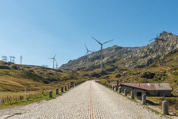 Historic Gotthard Pass road with cobblestones, wind turbines and electricity pylons, renewable...