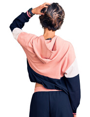 Young beautiful woman wearing sportswear backwards thinking about doubt with hand on head